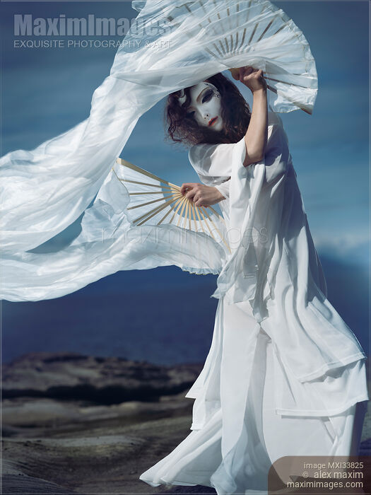 Mysterious asian woman in oriental theatrical face mask and flowy white dress dancing gracefully with silk fans